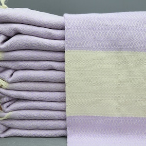 May include: A stack of lavender Turkish towels with a white stripe. The towels have a fringe on the ends.