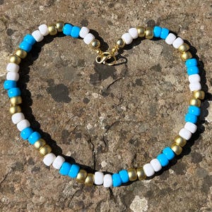 May include: A gold, white, and blue beaded necklace with a gold clasp.