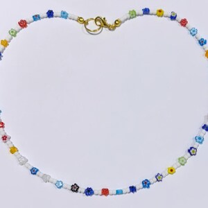 Puede incluir: Un collar de cuentas blancas con cuentas de colores en forma de flor. El collar tiene un cierre dorado.