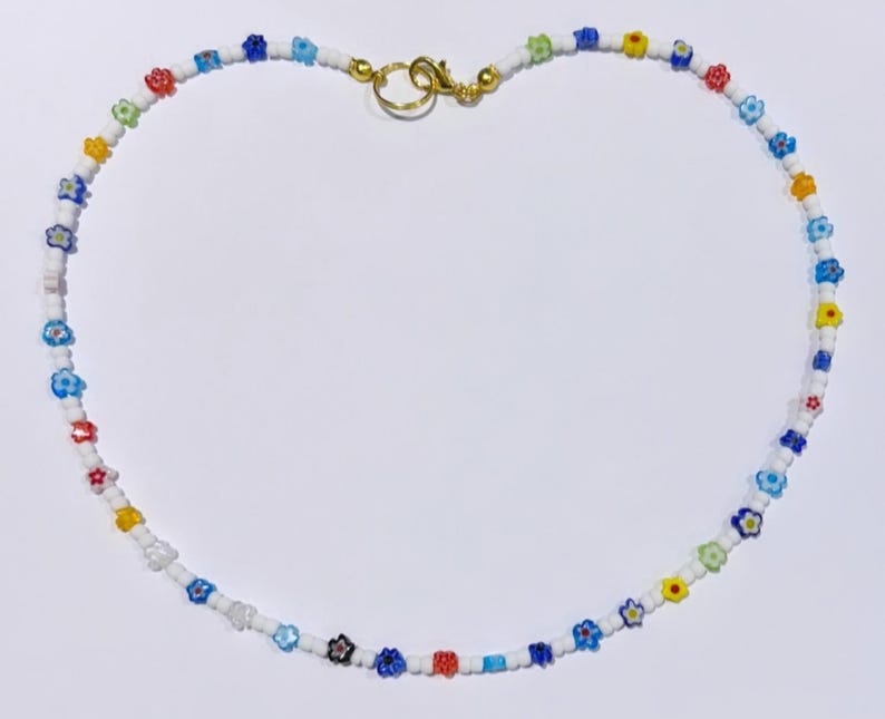 Puede incluir: Un collar de cuentas blancas con cuentas de colores en forma de flor. El collar tiene un cierre dorado.