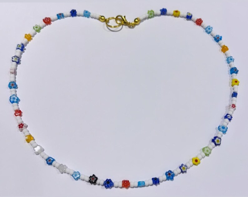 Puede incluir: Un collar de cuentas blancas con peque&ntilde;as cuentas de colores en forma de flor. El collar tiene un cierre dorado.
