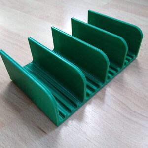 May include: A green plastic organizer with five slots for holding items. The organizer has a ridged bottom and rounded edges.
