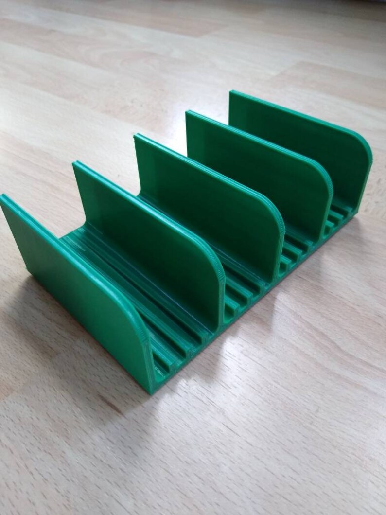 May include: A green plastic organizer with five slots for holding items. The organizer has a ridged bottom and rounded edges.