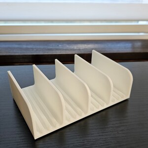 May include: White plastic organizer with five slots for holding items. The organizer is on a dark wood surface.