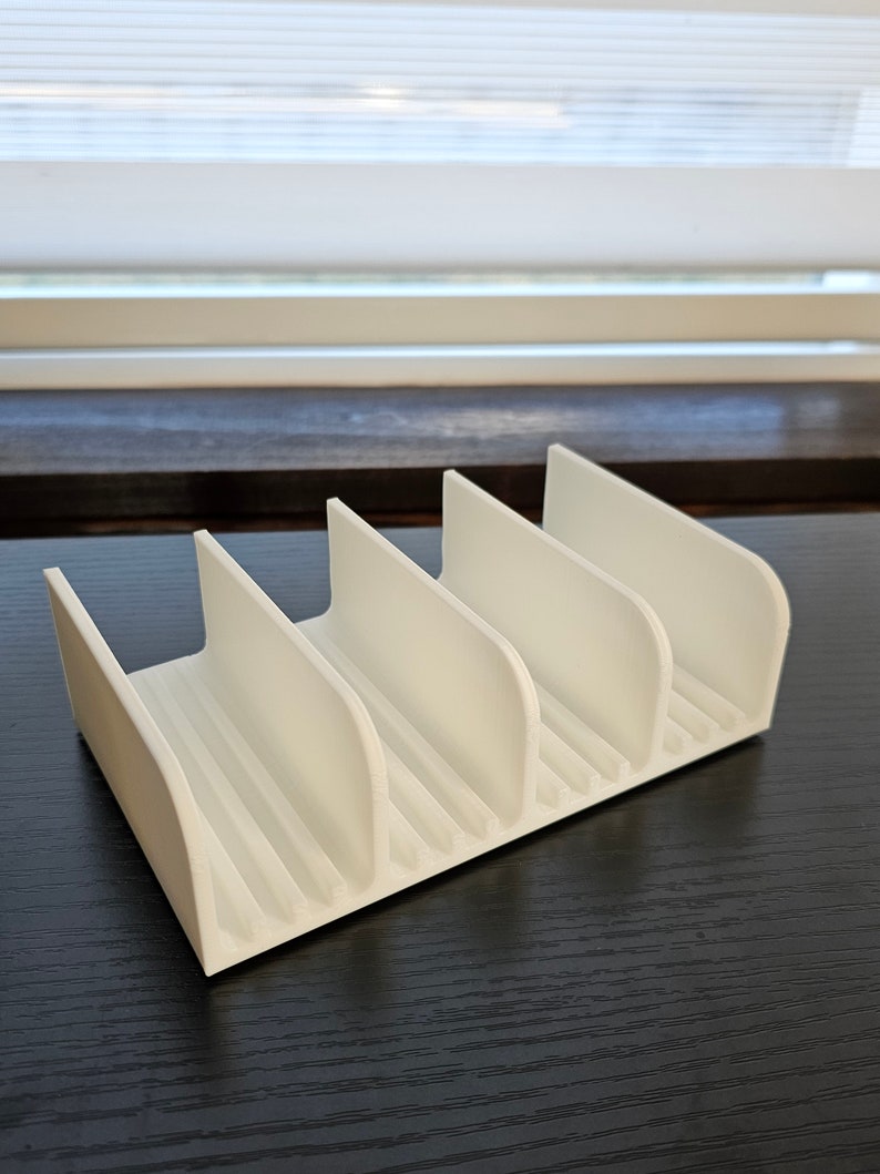 May include: White plastic organizer with five slots for holding items. The organizer is on a dark wood surface.