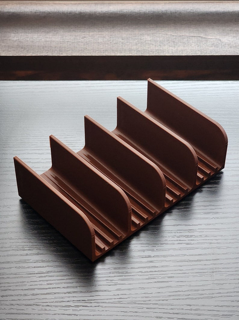 May include: A brown plastic organizer with five slots for storing items. The organizer has a textured surface and is designed to hold items upright.