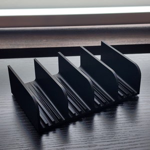 May include: Black plastic organizer with five slots for storing items. The organizer has a ribbed texture and a curved design.