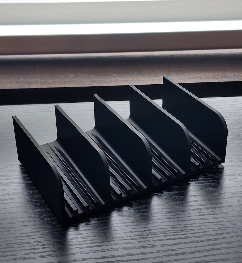 May include: Black plastic organizer with five slots for storing items. The organizer has a ribbed texture and a curved design.