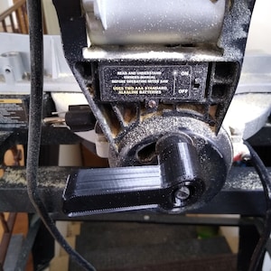 May include: Close-up of a black miter saw with a black lever and a label that reads "READ AND UNDERSTAND OWNERS MANUAL BEFORE OPERATING MITER SAW USES TWO AAA STANDARD ALKALINE BATTERIES ON OFF".