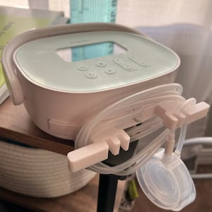May include: A white and light green electric breast pump with a digital display and multiple buttons. The pump has clear tubing and a white plastic connector.