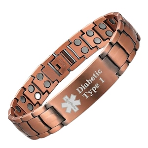 May include: A copper-colored bracelet with a rectangular link design. The bracelet has a medical ID plate with the words "Diabetic Type 1" and a medical symbol. The word "Copper" is stamped on the clasp.