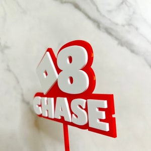 Peut inclure: Un topper de g&acirc;teau rouge et blanc avec le chiffre 8 et le nom Chase. Le chiffre 8 est dans un carr&eacute; blanc avec un contour rouge. Le nom Chase est en lettres blanches avec un contour rouge.