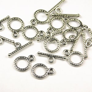 May include: Silver-toned metal toggle clasps with a twisted rope design. The clasps have a round ring on one end and a bar with a small ring on the other end.