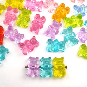 May include: Assortment of colourful gummy bear charms in various colours, including red, orange, yellow, green, blue, and purple. The charms are arranged on a white surface.