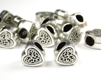 May include: A group of silver heart-shaped beads with an intricate design. The beads have a hole in the centre for threading onto a bracelet or necklace.