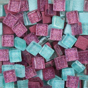 May include: A close-up of a collection of small, square mosaic tiles. The tiles are a mix of light blue and pink with glitter accents.