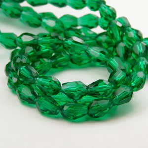 May include: A strand of emerald green faceted glass beads. The beads are oval shaped and have a high shine.