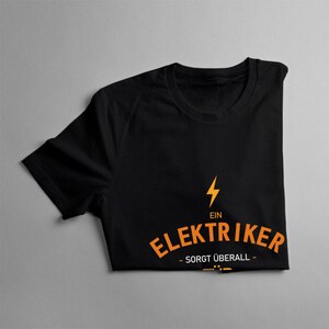 Puede incluir: Camiseta negra con un rayo naranja y el texto "EIN ELEKTRIKER - Sorgt &uuml;berall -"