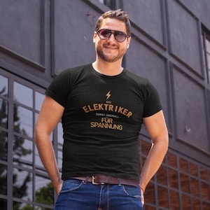 Puede incluir: Una camiseta negra con un gr&aacute;fico de rayo dorado y el texto "Ein Elektriker - sorgt &uuml;berall - f&uuml;r Spannung".