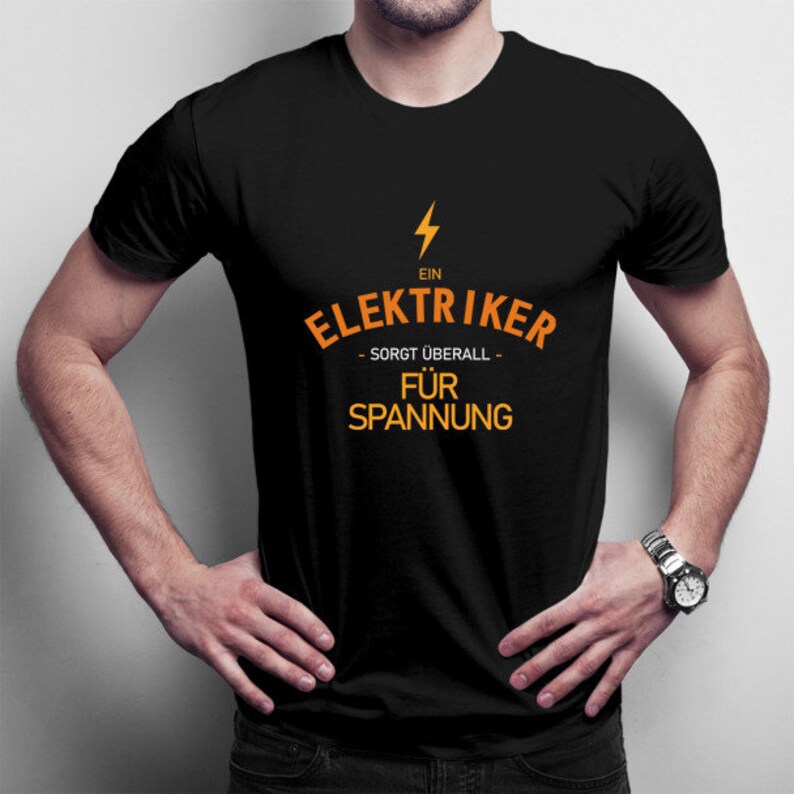Puede incluir: Una camiseta negra con un gr&aacute;fico naranja que dice "Ein Elektriker - sorgt &uuml;berall - f&uuml;r Spannung".