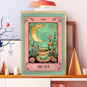 Peut inclure: Une impression d'art encadr&eacute;e repr&eacute;sentant une carte de tarot. L'&oelig;uvre d'art repr&eacute;sente un croissant de lune, des fleurs et une tasse de th&eacute;, avec les mots "THE TEA" en bas. Le cadre est marron clair et la carte a une bordure rose et verte.