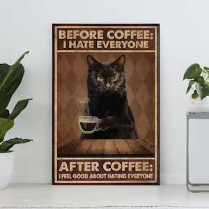 Op de afbeelding: Een ingelijste poster met een zwarte kat die een kopje koffie vasthoudt. De tekst luidt "BEFORE COFFEE: I HATE EVERYONE" en "AFTER COFFEE: I FEEL GOOD ABOUT HATING EVERYONE". De achtergrond is een bruin ruitpatroon.