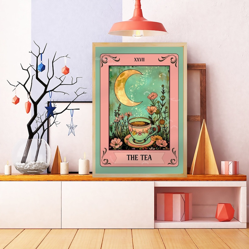 Peut inclure: Une impression d'art encadr&eacute;e repr&eacute;sentant une carte de tarot. L'&oelig;uvre d'art repr&eacute;sente un croissant de lune, des fleurs et une tasse de th&eacute;, avec les mots "THE TEA" en bas. Le cadre est marron clair et la carte a une bordure rose et verte.