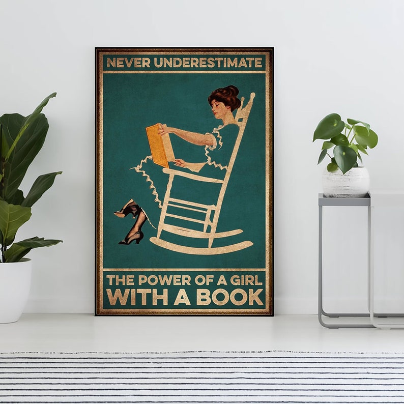 May include: A framed poster with the text "NEVER UNDERESTIMATE THE POWER OF A GIRL WITH A BOOK." The image depicts a woman in a rocking chair reading a book. The background is teal with gold accents.