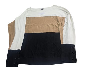 May include: A color block sweater with a white, tan, and black design. The long sleeves are white, and the cuffs are black with decorative lacing. The sweater has a round neckline and a tag attached.