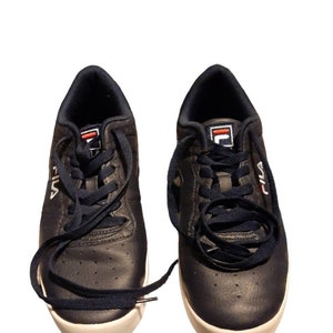 May include: A pair of navy blue Fila sneakers with white soles. The sneakers have navy blue laces and the Fila logo in white and red on the tongue and side. The shoes are set against a white background.
