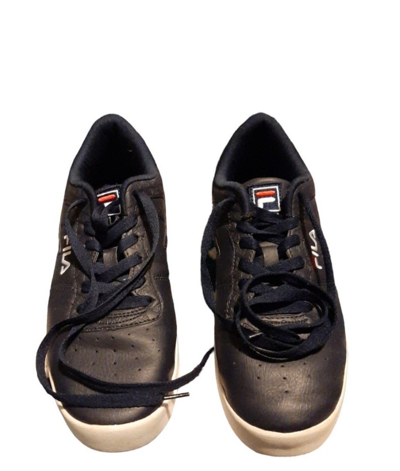 May include: A pair of navy blue Fila sneakers with white soles. The sneakers have navy blue laces and the Fila logo in white and red on the tongue and side. The shoes are set against a white background.
