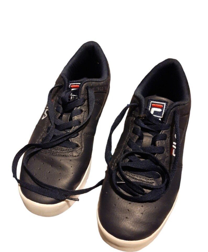 May include: A pair of navy blue Fila sneakers with white soles and navy blue laces. The sneakers have the Fila logo in white and red on the tongue and side. The shoes are made of a leather-like material.