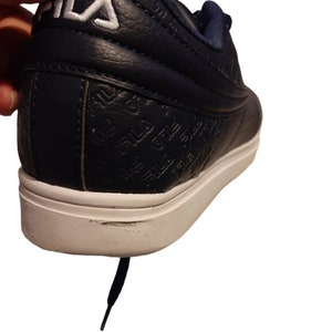 May include: Navy blue athletic shoe with white sole. The shoe features the brand name "FILA" in white on the heel and embossed on the side. The shoe has a white sole and a navy blue lace.