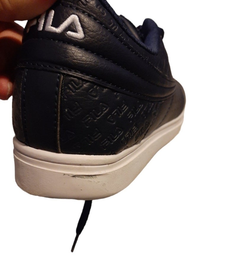 May include: Navy blue athletic shoe with white sole. The shoe features the brand name "FILA" in white on the heel and embossed on the side. The shoe has a white sole and a navy blue lace.
