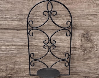 May include: Black metal wall sconce with an arched top and decorative scrollwork. The sconce has a circular base for a candle. The design is a classic, elegant style for home decor.