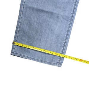 Puede incluir: Vaqueros de mezclilla azul claro con una cinta m&eacute;trica amarilla que muestra una medida de aproximadamente 30 cm. Los vaqueros tienen un dise&ntilde;o cl&aacute;sico de cinco bolsillos y est&aacute;n hechos de una tela de mezclilla duradera.