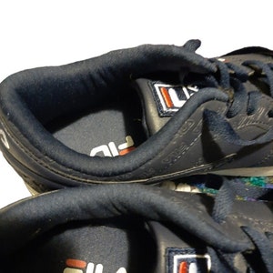 May include: Close-up of navy blue athletic shoes. The shoes feature the brand name "FILA" in white with a red accent. The interior of the shoe is navy blue, and the exterior has the brand name printed on the side.