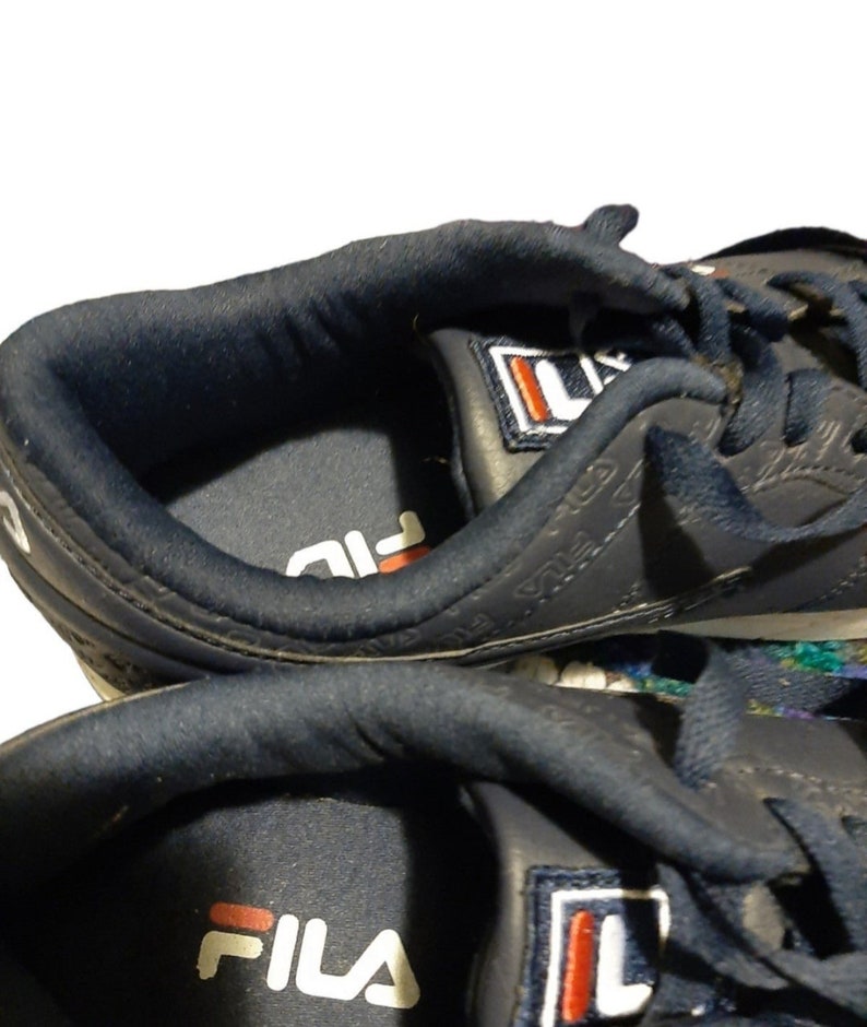 May include: Close-up of navy blue athletic shoes. The shoes feature the brand name "FILA" in white with a red accent. The interior of the shoe is navy blue, and the exterior has the brand name printed on the side.