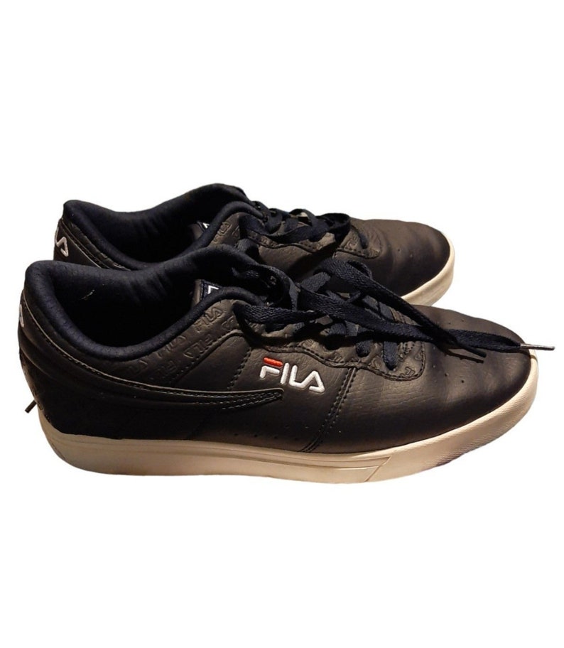 May include: A pair of navy blue Fila sneakers with white soles and laces. The Fila logo is displayed in white with a red accent. The shoes have a low-profile design and are made of a textured material.