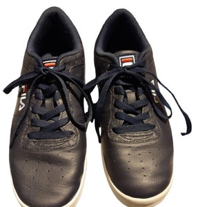 May include: A pair of navy blue Fila sneakers with white soles. The sneakers have navy blue laces and the Fila logo in white on the side. The tongue features the Fila logo in red and white.