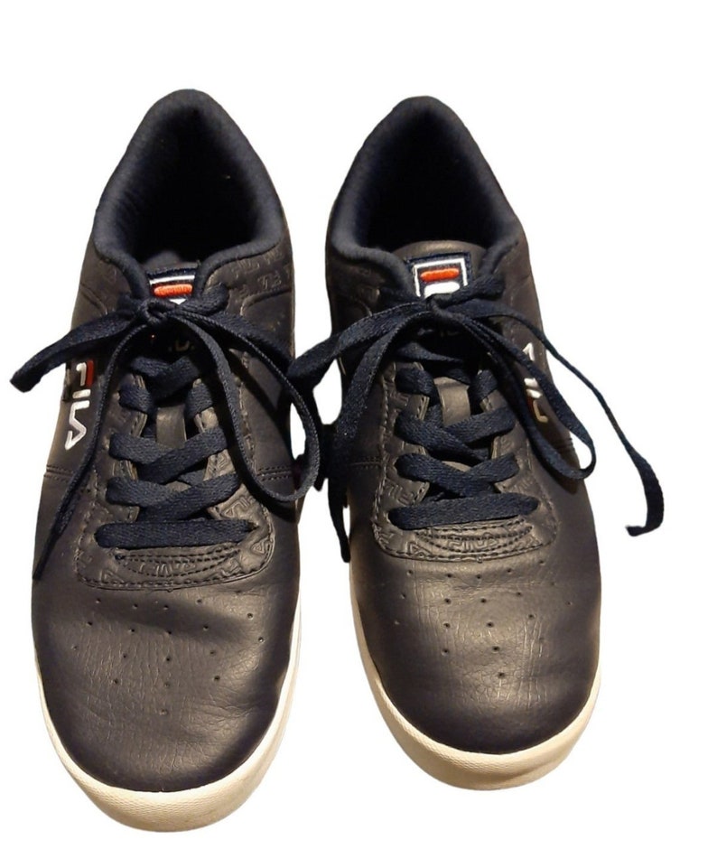 May include: A pair of navy blue Fila sneakers with white soles. The sneakers have navy blue laces and the Fila logo in white on the side. The tongue features the Fila logo in red and white.