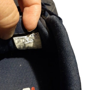 May include: Close-up of a navy blue Fila athletic shoe. The shoe's interior label displays size information: US 8.5, EUR 41, UK 7.5, and MEX 26.5. The shoe is made in China.