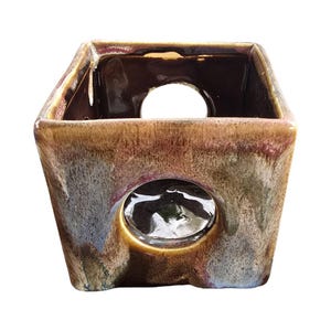 May include: A square ceramic planter with a unique design. The planter features a dark brown, tan, and purple glaze with a hole in the front and top. The planter is suitable for small plants or succulents.