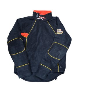May include: Black fleece jacket with a high collar and a zip closure. The jacket features orange and yellow accents, including a logo patch on the sleeve and embroidered details. The jacket has a drawstring at the bottom.