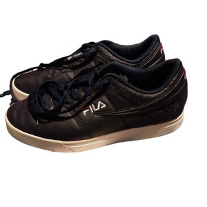 May include: A pair of navy blue Fila sneakers with white soles and navy blue laces. The Fila logo is in white with a red accent. The sneakers have a low-profile design and are made of leather.