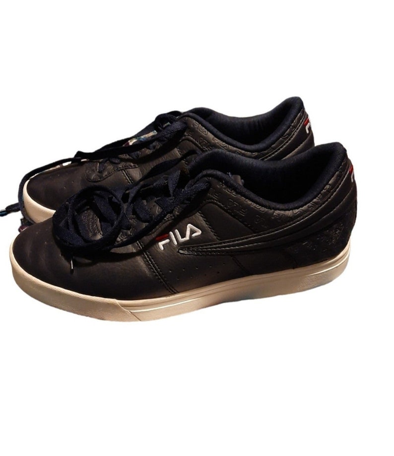 May include: A pair of navy blue Fila sneakers with white soles and navy blue laces. The Fila logo is in white with a red accent. The sneakers have a low-profile design and are made of leather.