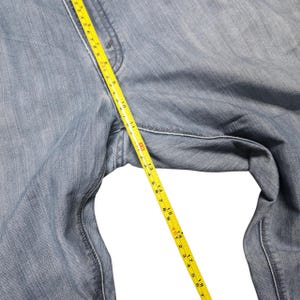 Puede incluir: Vaqueros de mezclilla azul claro con una cinta m&eacute;trica amarilla que muestra una medida de aproximadamente 46 cm. Los vaqueros est&aacute;n hechos de mezclilla de lavado claro y son parcialmente visibles.