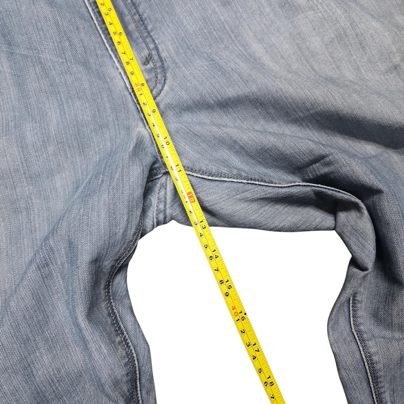 Puede incluir: Vaqueros de mezclilla azul claro con una cinta m&eacute;trica amarilla que muestra una medida de aproximadamente 46 cm. Los vaqueros est&aacute;n hechos de mezclilla de lavado claro y son parcialmente visibles.