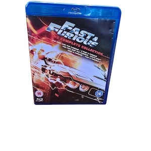 May include: A blue Blu-ray case with a black and red image of a car. The case has the title "Fast & Furious: The Complete Collection" and lists the titles of the movies included: "The Fast and the Furious", "2 Fast 2 Furious", "The Fast and the Furious: Tokyo Drift", "Fast & Furious", and "Fast & Furious 5".