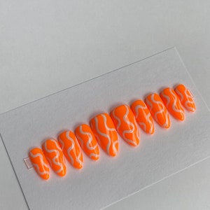 May include: Set of ten orange press-on nails with white abstract swirl designs.
